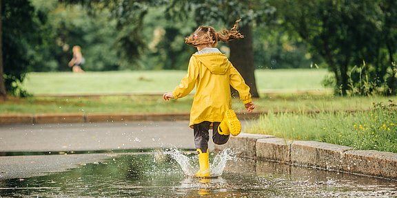 Ratgeber Immunsystem Stärken Kind mit gelber Regenjacke springt in Pfütze